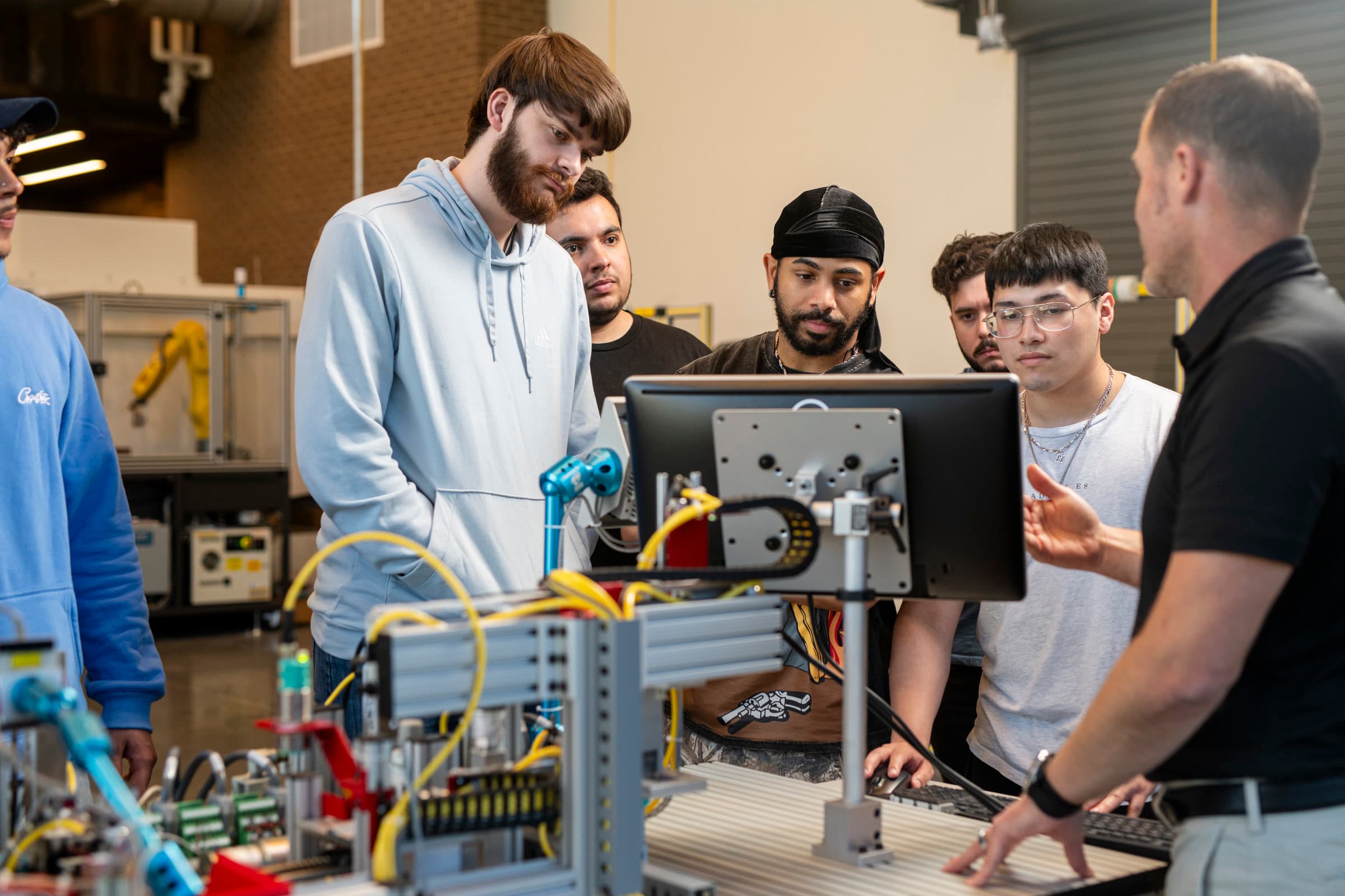 Students gathered around automation equipment as an instructor explains it